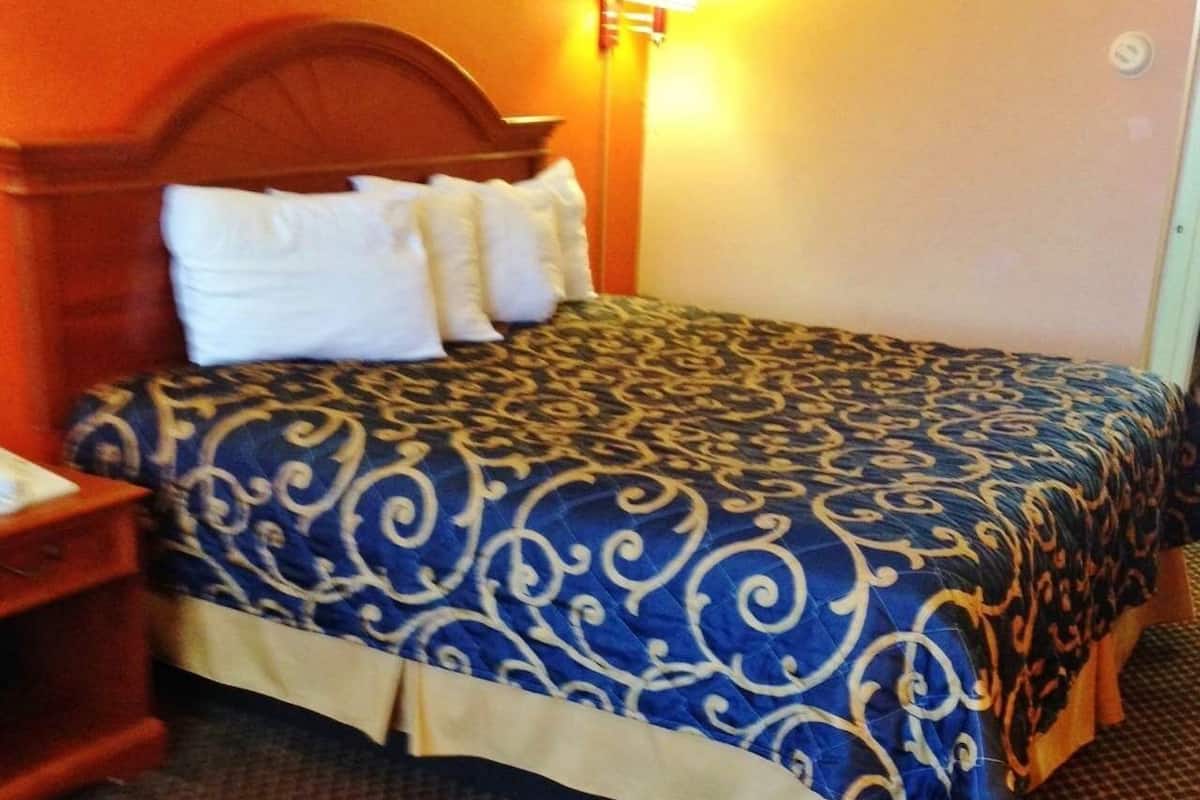 A hotel room with a bed, a nightstand, and a lamp.