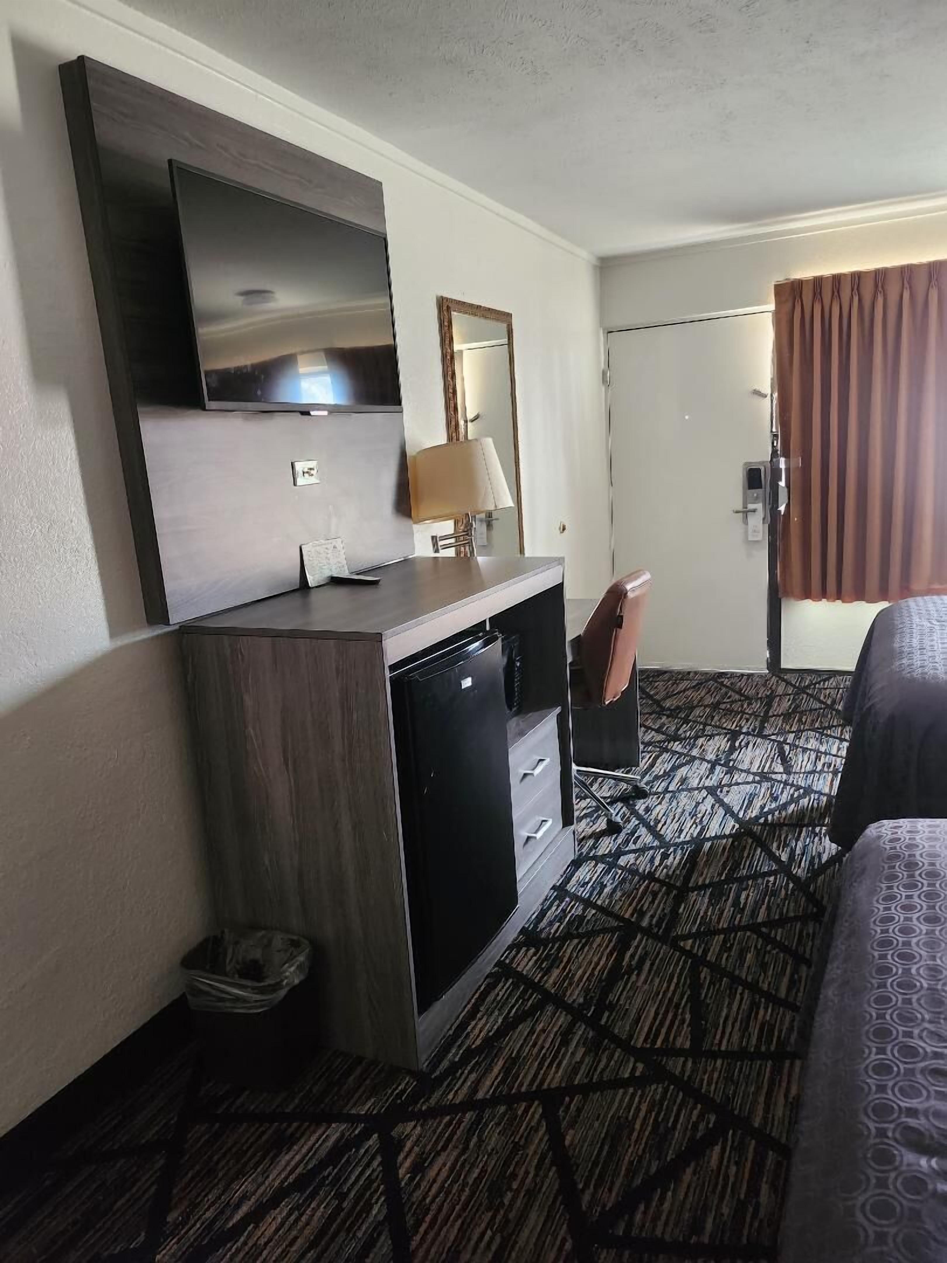 Una camera d'albergo con un letto, una scrivania con televisore, uno specchio e un tappeto a motivi.