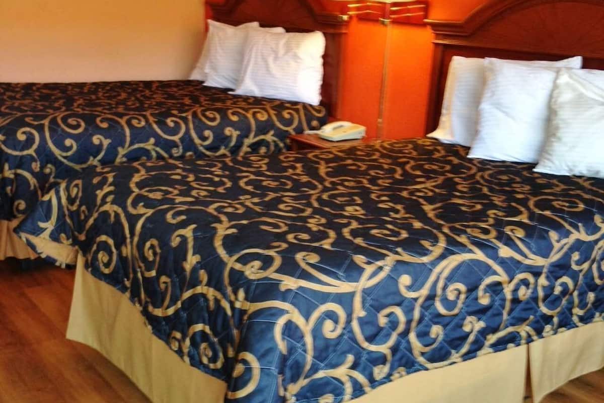 Two double beds with matching blue and gold patterned bedspreads, a bedside table with a lamp, and a wall socket.