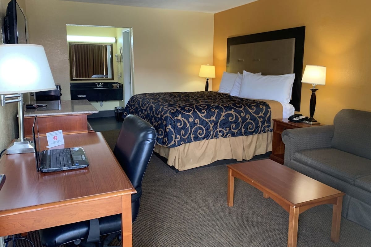 A hotel room with a bed, two bedside lamps, a desk with a laptop, a chair, a sofa, and a small table.