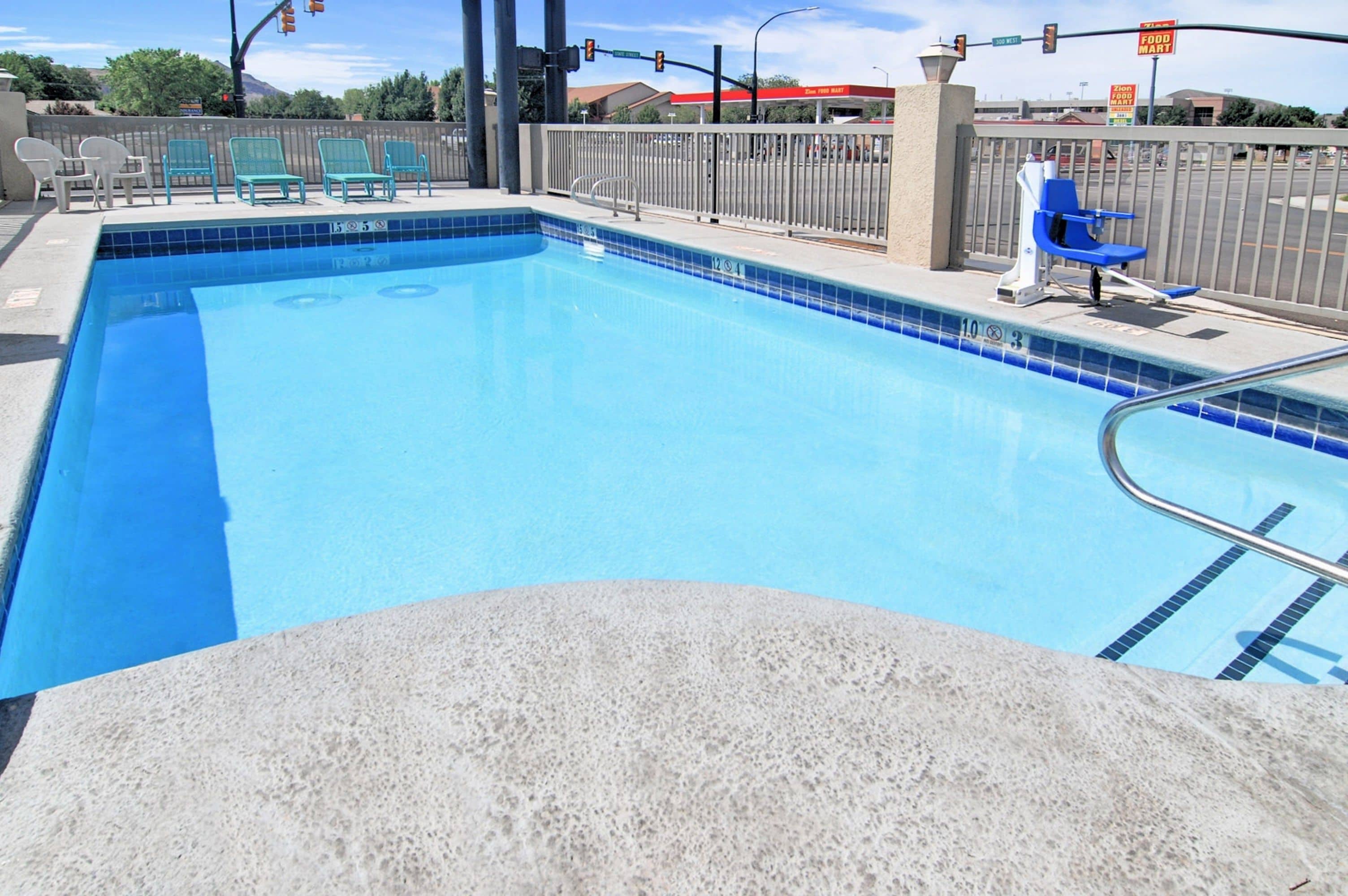 Une piscine rectangulaire aux carreaux bleus, avec un escalier en métal et plusieurs chaises longues.