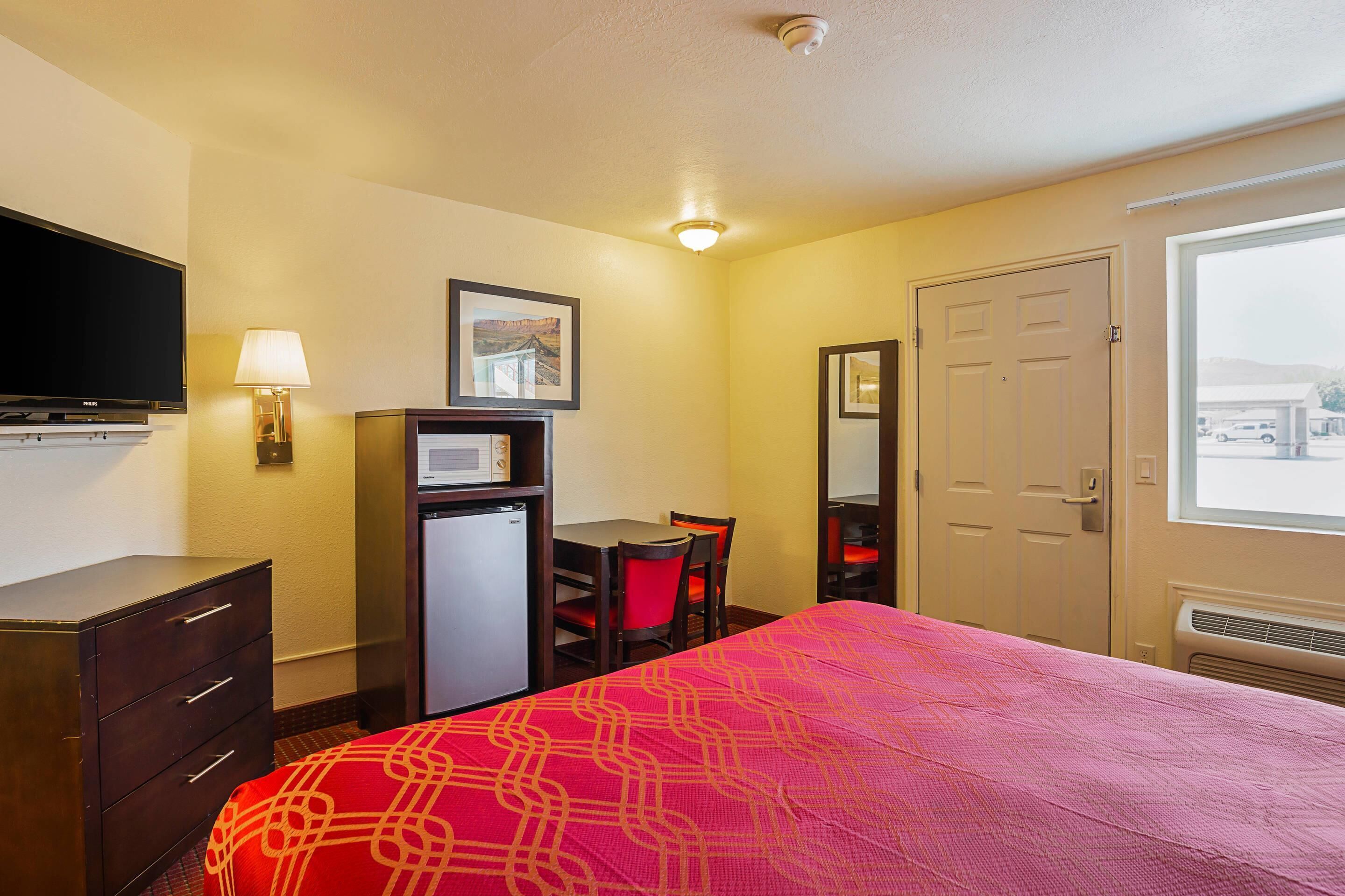 A hotel room with a bed, a desk, a chair, a television, a refrigerator, and a window with a view.