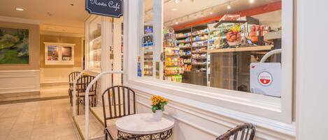 A cafe with a sign reading "Mens Café," a window view of the interior, and a small table with chairs outside.