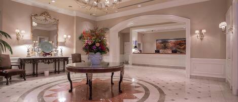 A lobby with a round table, a chandelier, a large mirror, and a reception desk.