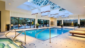 An indoor swimming pool with clear glass walls, a skylight, and a wooden deck area with lounge chairs. - The Sutton Place Hotel Vancouver (Vancouver)