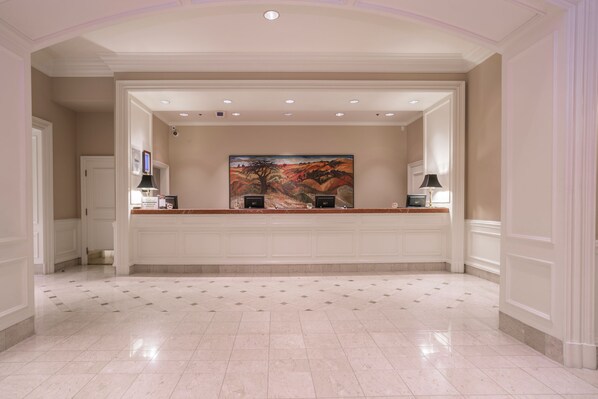 A reception area with a marble floor, a large painting on the wall, and a counter with two lamps. - The Sutton Place Hotel Vancouver (Vancouver)