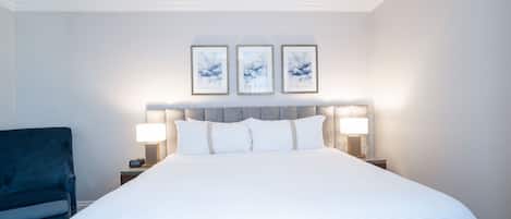 A hotel room with a large bed, two bedside lamps, a headboard with three framed artworks, and a blue armchair.