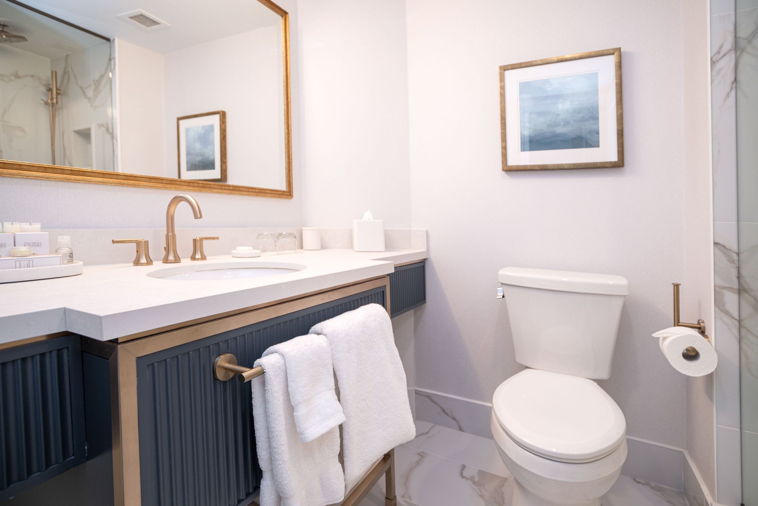 Une salle de bain moderne avec un lavabo blanc, des robinets dorés, des toilettes et un tableau encadré au mur.
