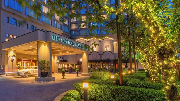 A hotel entrance with a covered walkway, a well-maintained garden, and illuminated trees. - The Sutton Place Hotel Vancouver (Vancouver)