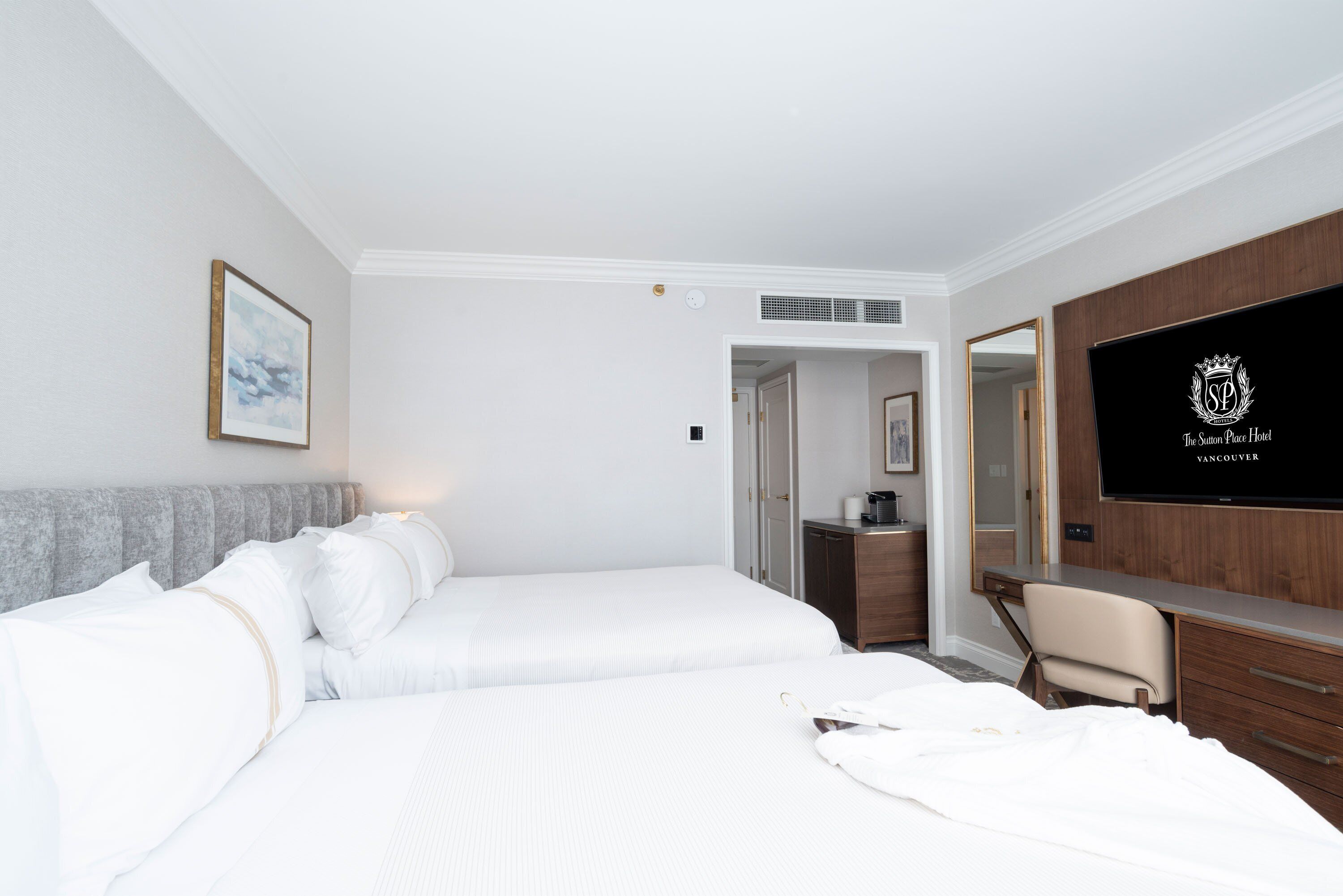A hotel room with two beds, a desk, a chair, a television, and a framed picture on the wall.