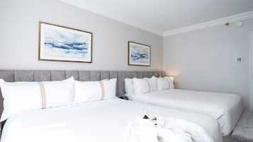 Una habitación de hotel con dos camas, cabecera gris, ropa de cama blanca y dos cuadros en la pared.