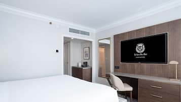 A hotel room with a large bed, a desk with a chair, a flat-screen TV mounted on the wall, and a wooden wardrobe.
