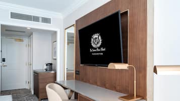 Una habitación de hotel moderna con un televisor de pantalla plana montado en una pared de madera, un escritorio con una silla y una mesita redonda pequeña.