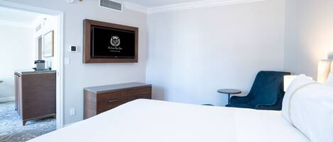 A hotel room with a large bed, a dresser, a chair, and a framed sign on the wall.