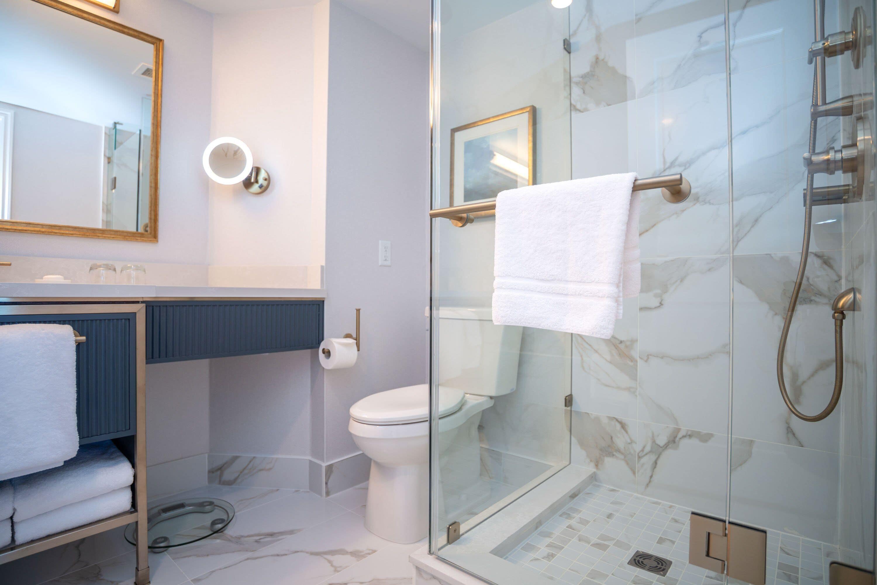 A modern bathroom with a glass-enclosed shower, a toilet, and a sink with a towel rack.