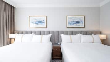 Une chambre d’hôtel avec deux lits, une tête de lit grise en tissu, du linge de lit blanc et deux tableaux abstraits encadrés accrochés au mur.