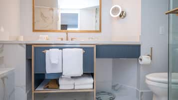 A modern bathroom with a marble floor, a vanity with a blue cabinet, a glass shower enclosure, and a large mirror with a gold frame.