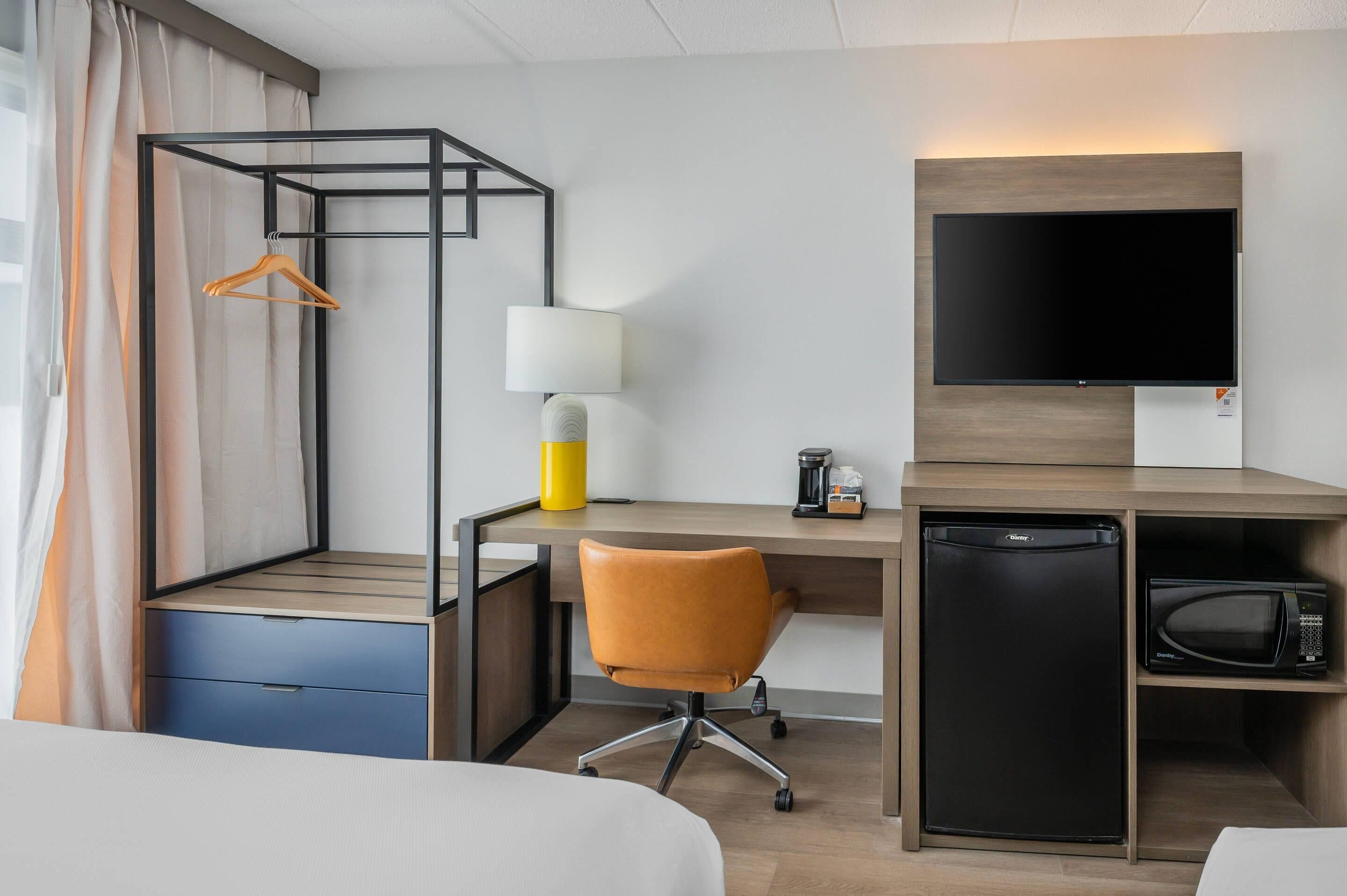 A hotel room with a bed, a desk with a chair, a TV, a mini-fridge, and a microwave.