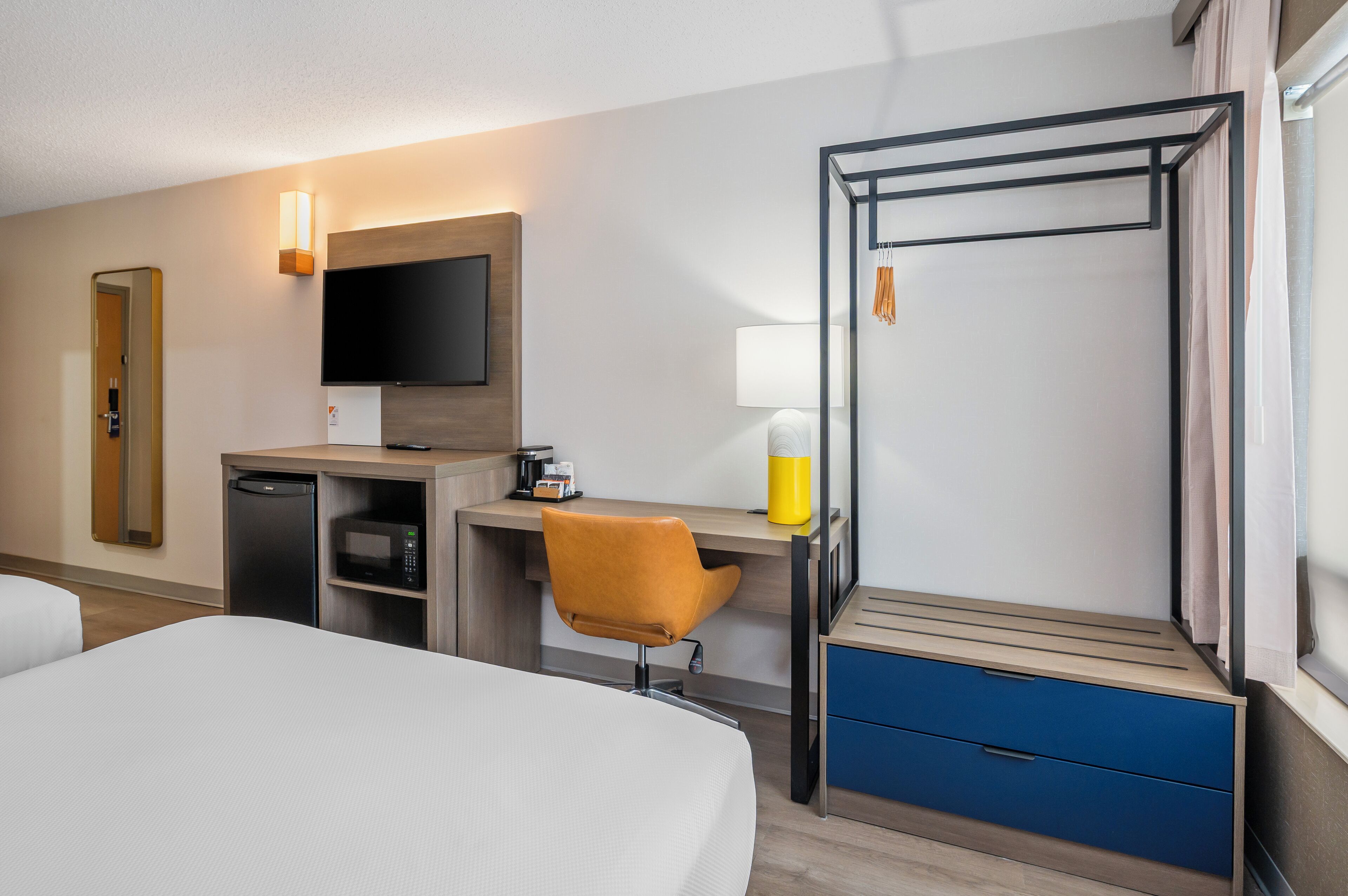 Una habitación de hotel con cama, escritorio con computadora, televisor, microondas y una pequeña cocina.