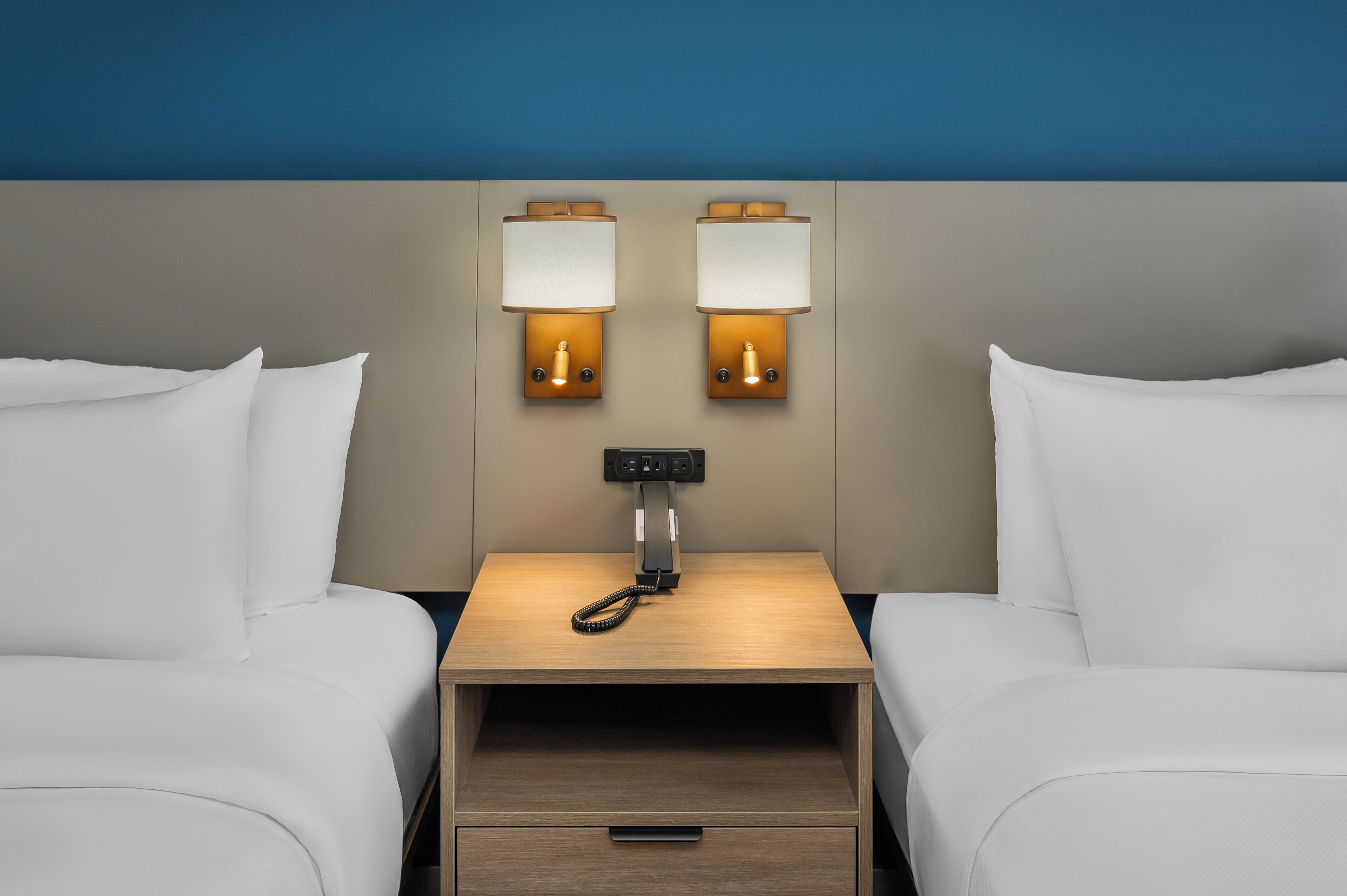 Ett hotellrum med två sängar, ett nattduksbord med en lampa och en kontrollpanel.