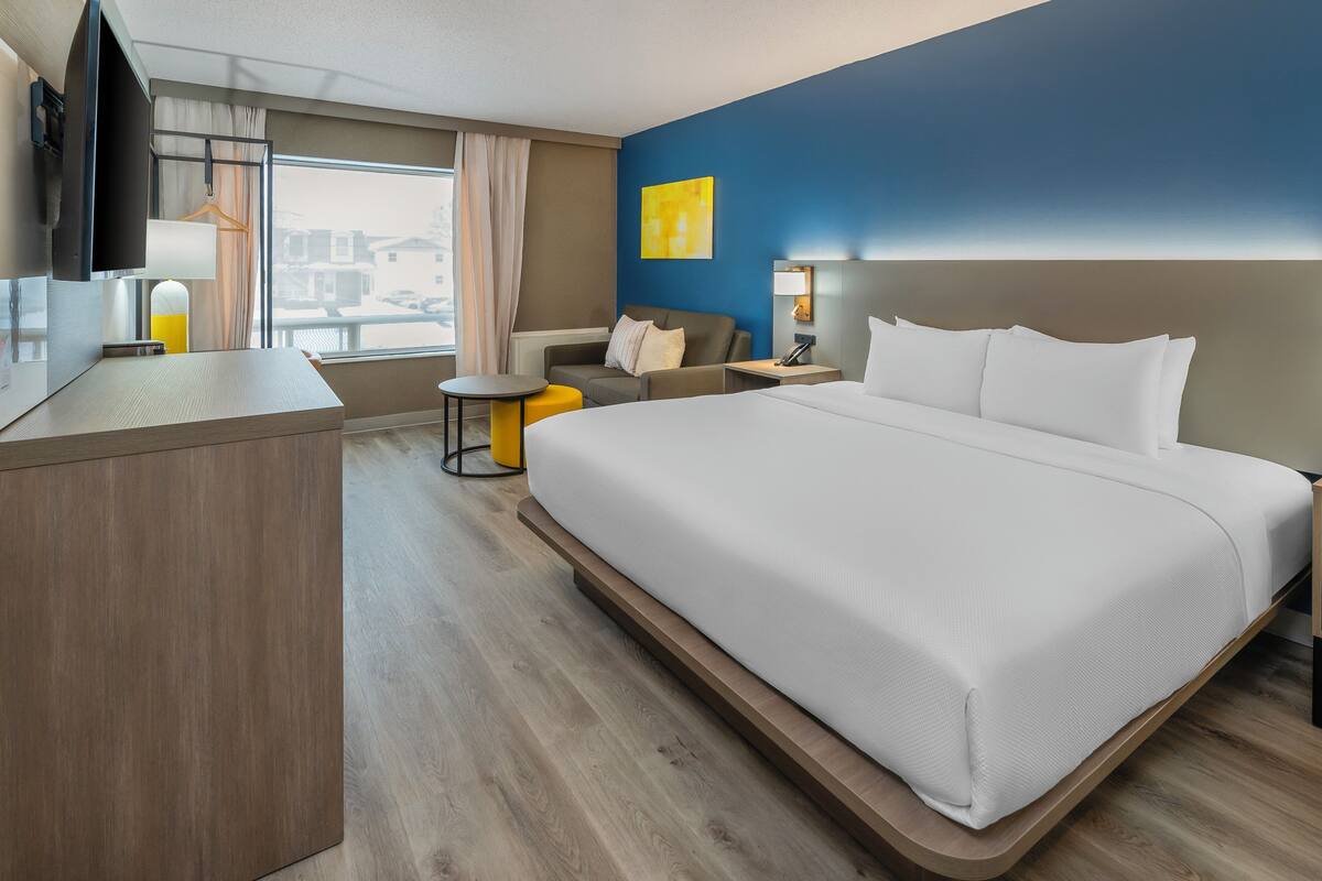 Une chambre d’hôtel avec un grand lit, un bureau, une chaise, une petite table et un téléviseur.