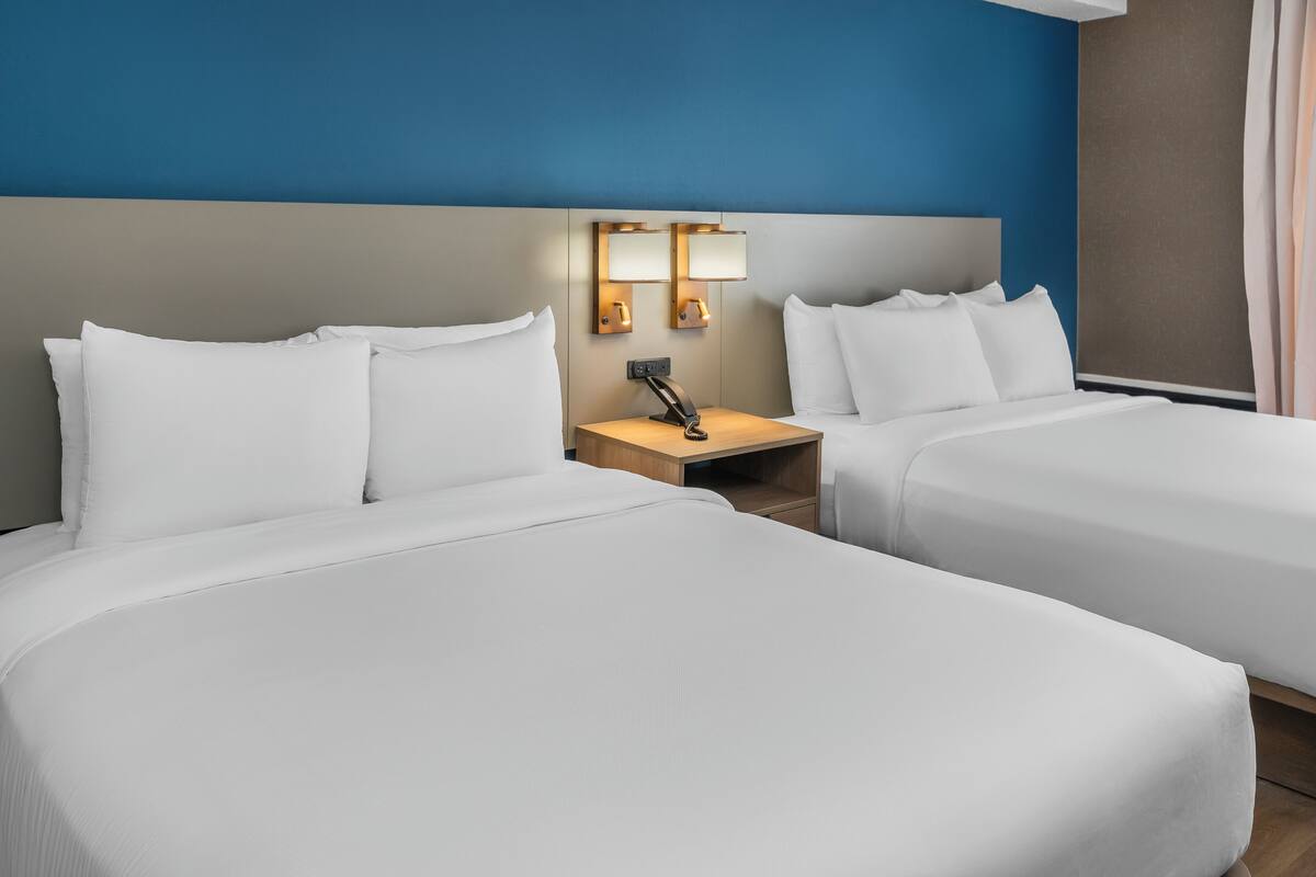 Une chambre d’hôtel avec deux lits, une table de chevet avec une lampe et un luminaire fixé au mur.
