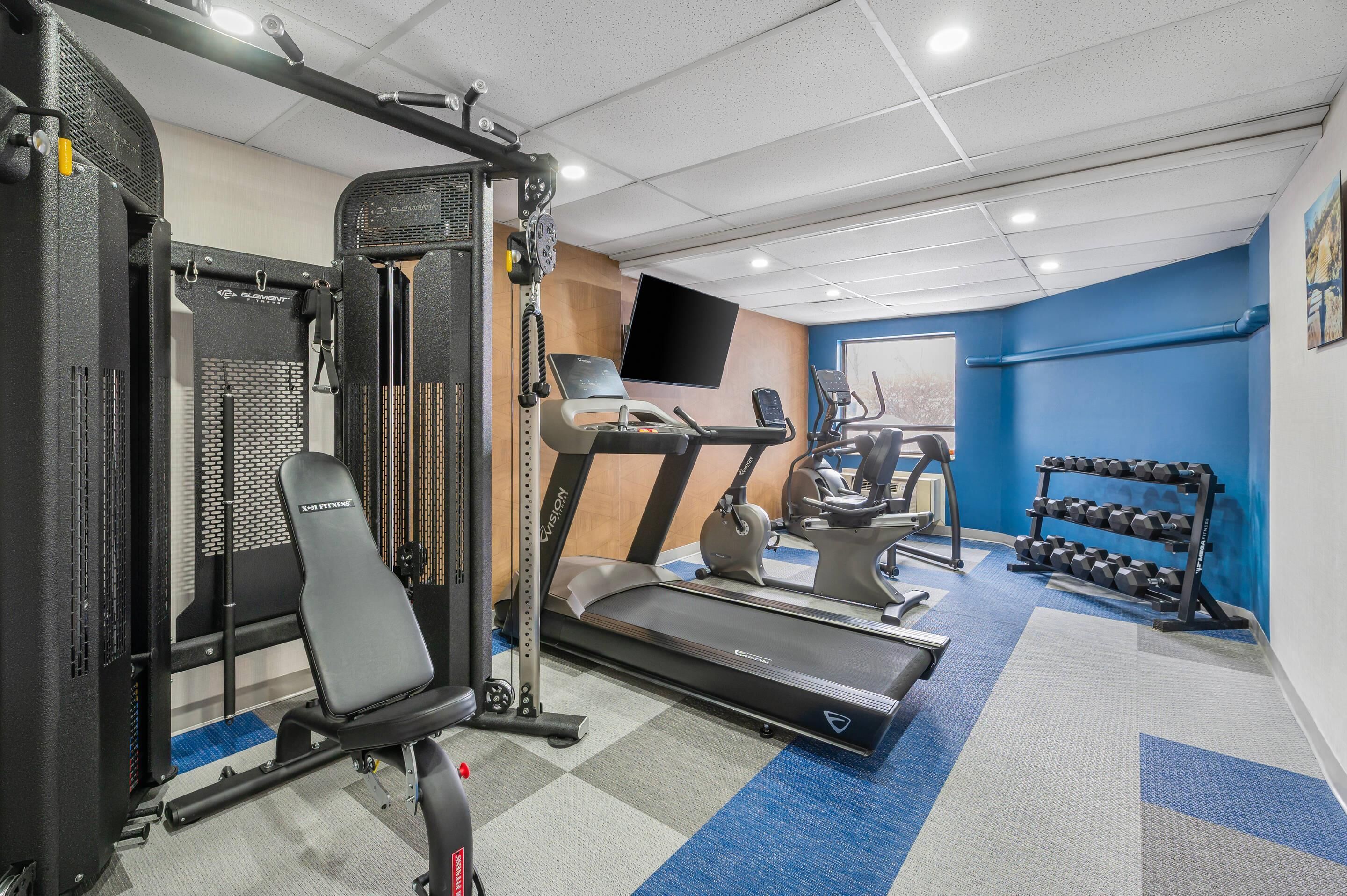 Un gimnasio con cinta de correr, banco para pesas y mancuernas.