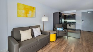 A modern living room with a sofa, a small round table, a lamp, and a kitchenette in the background. - Comfort Inn Belleville (Belleville)