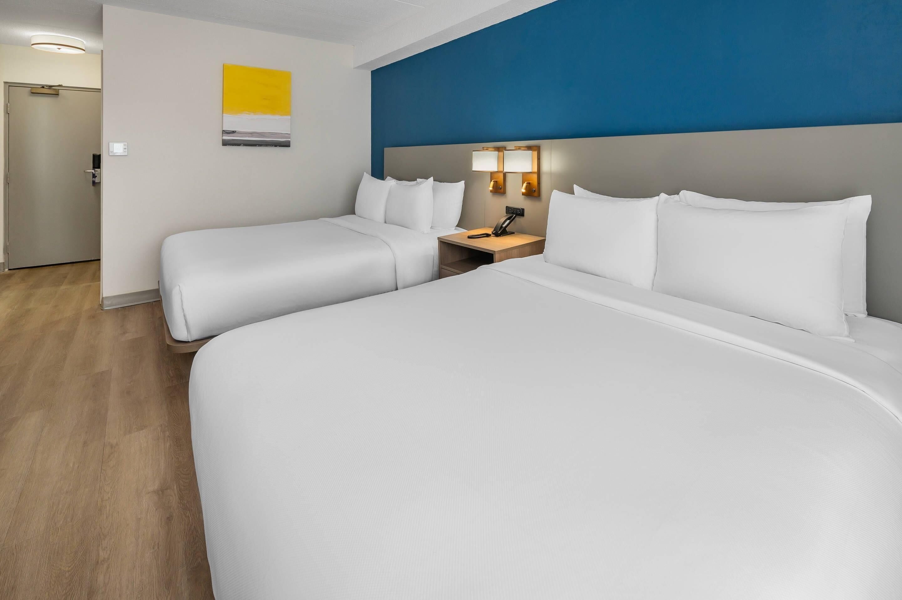 Una habitación de hotel con dos camas, una mesita de noche y una lámpara fijada a la pared.