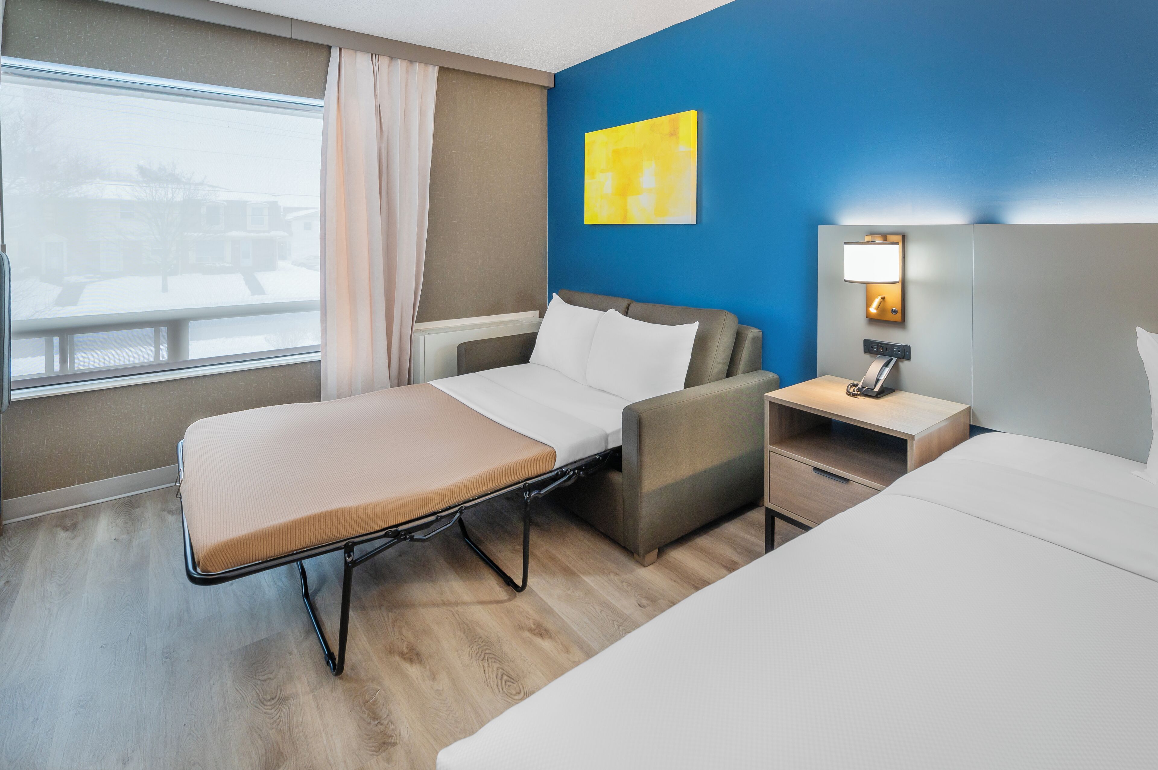 Una habitación de hotel con cama, una silla, una mesita de noche y una ventana con cortinas.
