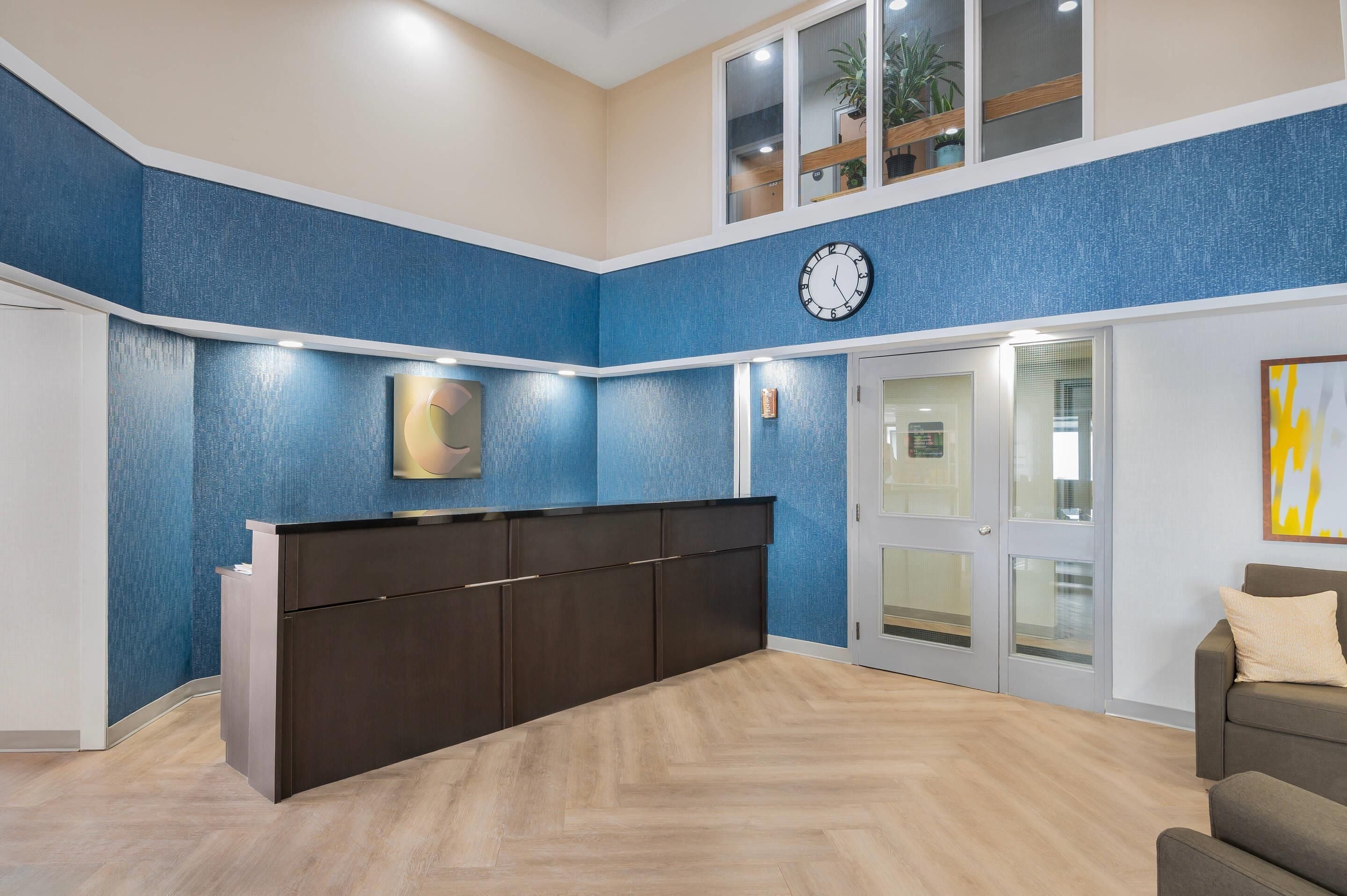 A reception area with a dark wooden desk, a clock, and a blue textured wall.