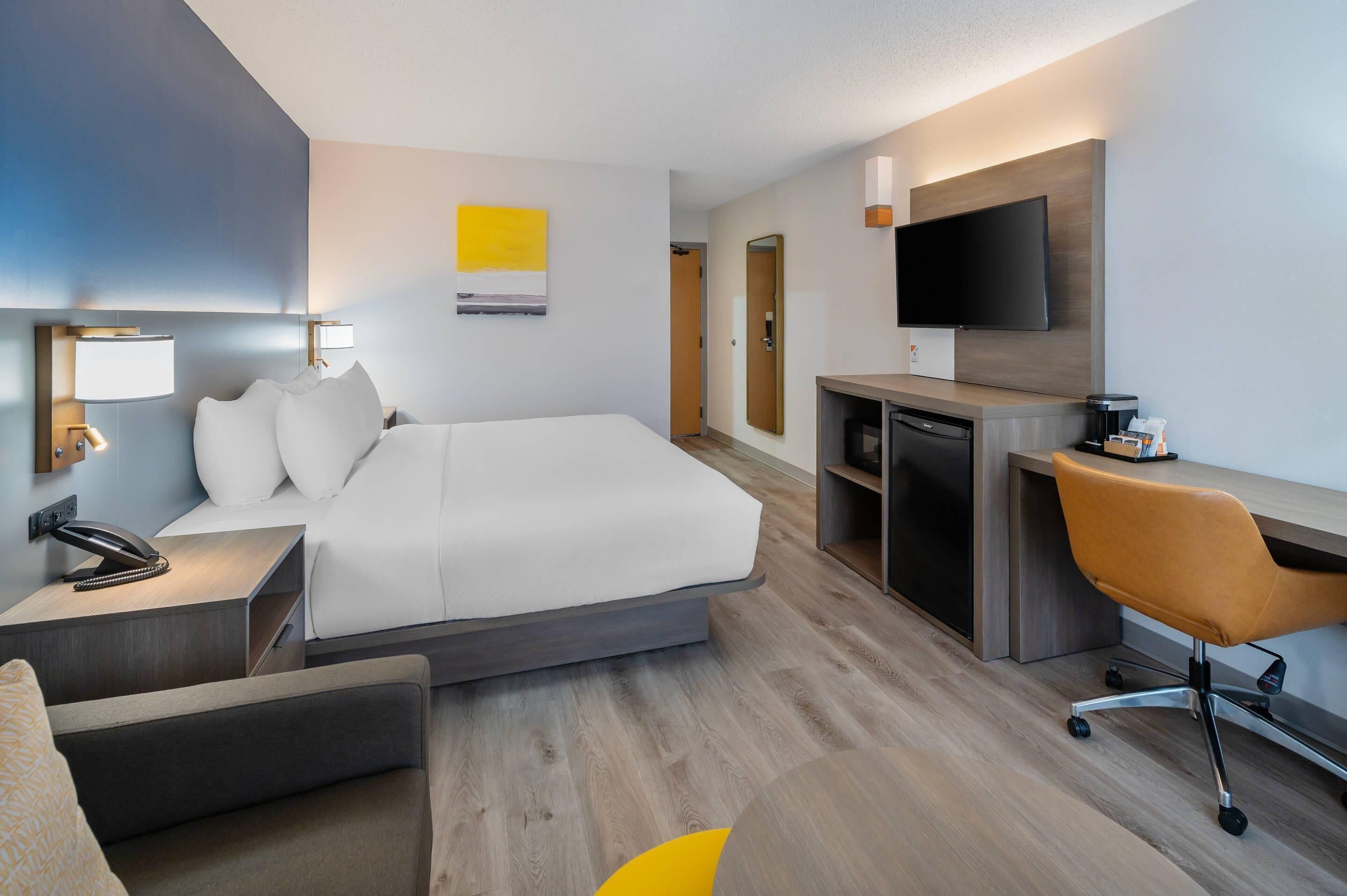 Ett modernt hotellrum med en säng, ett skrivbord, en stol och en TV.
