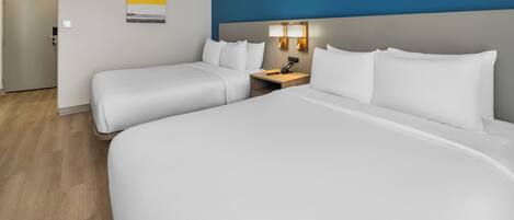 Habitación de hotel con dos camas, una mesita de noche con lámpara y una puerta.