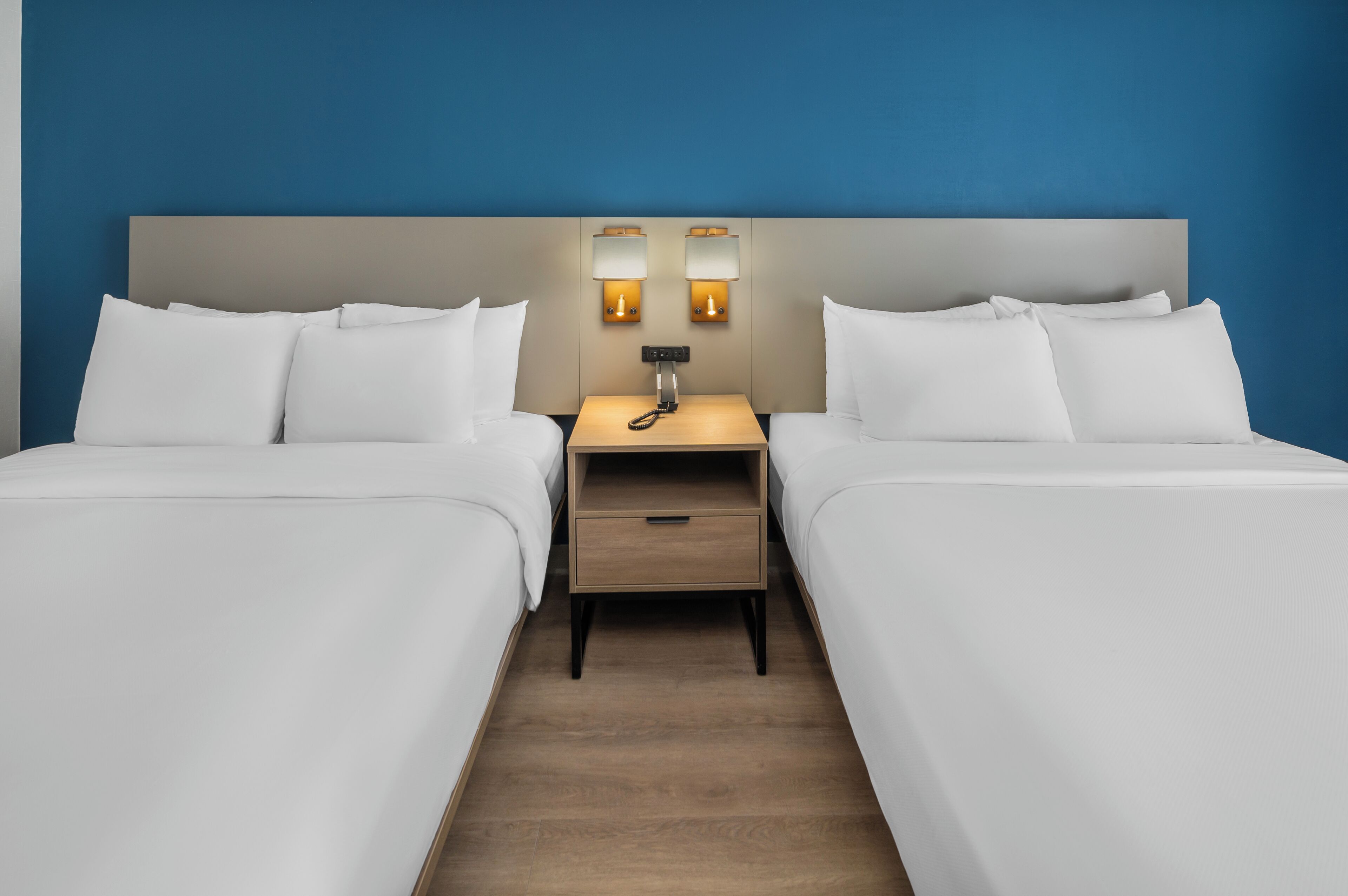 A hotel room with two beds, a nightstand with a lamp, and a wooden floor.
