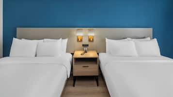 A hotel room with two beds, a nightstand with a lamp, and a wooden floor.