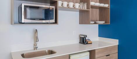 Una cocina moderna con microondas integrado, cafetera y lavabo.