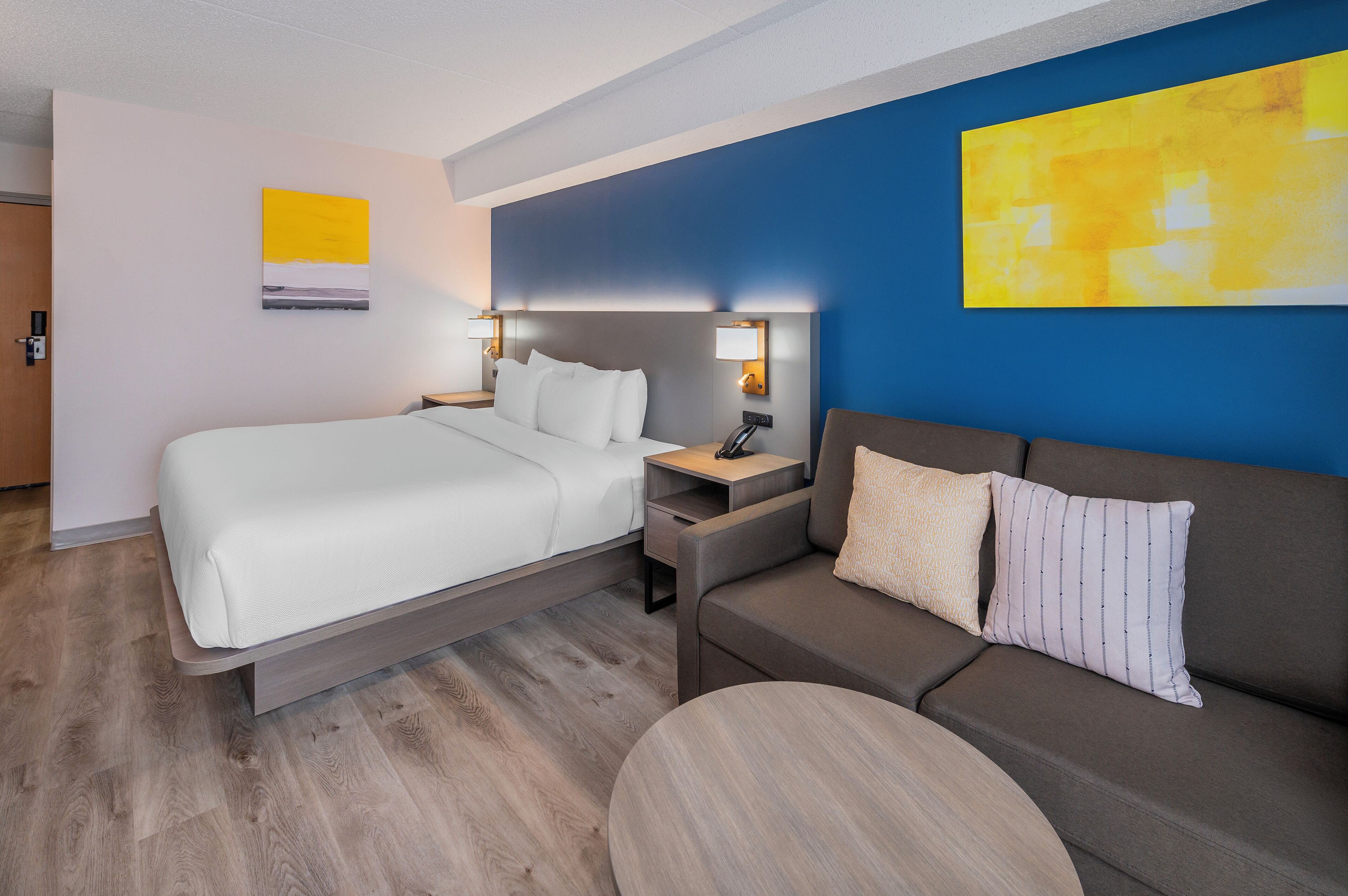 Una habitación de hotel con una cama, un sofá, una mesita de noche y una lámpara.