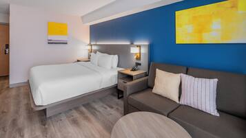 Una habitación de hotel con una cama, un sofá, una mesita de noche y una lámpara.