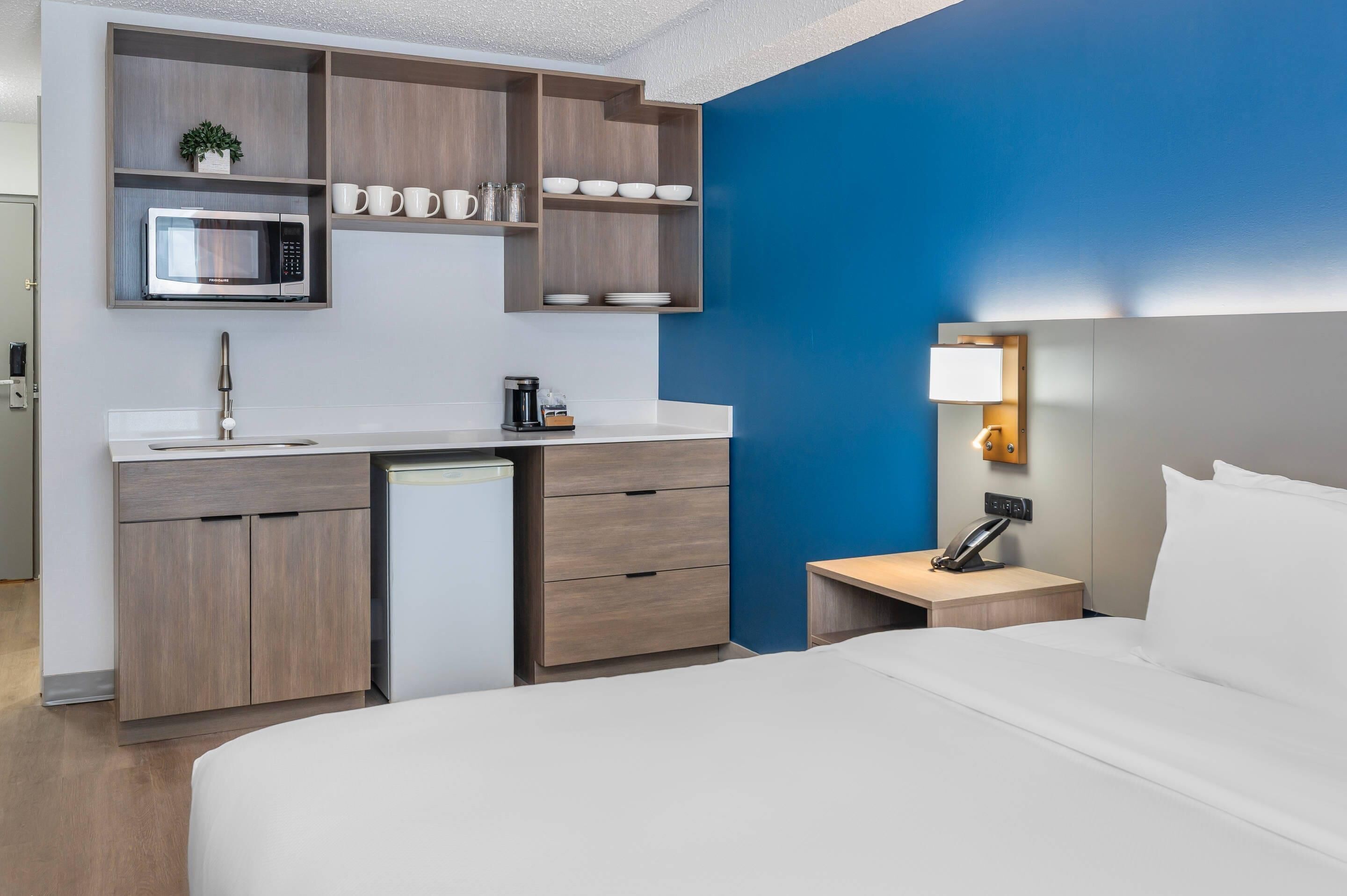A hotel room with a bed, a desk with a microwave, a coffee maker, and a small cabinet.