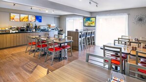 A modern dining area with wooden flooring, metal chairs with red cushions, and a central island with a kitchen counter. - Comfort Inn Belleville (Belleville)
