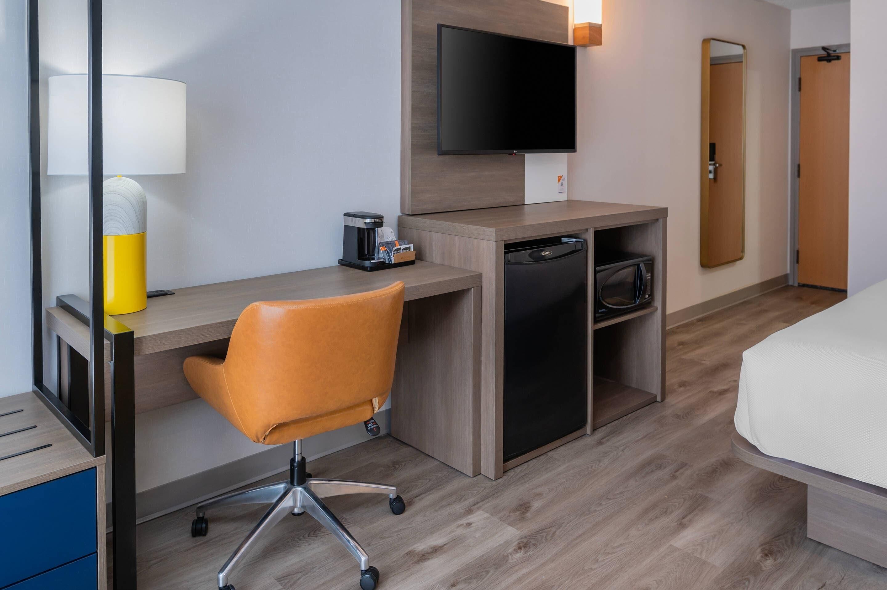 A hotel room with a desk, chair, television, and a bed.