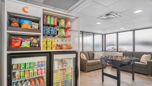 A kitchenette with a fridge stocked with beverages and snacks, a foosball table, and a sofa in a modern room with large windows. - Comfort Inn Belleville (Belleville)