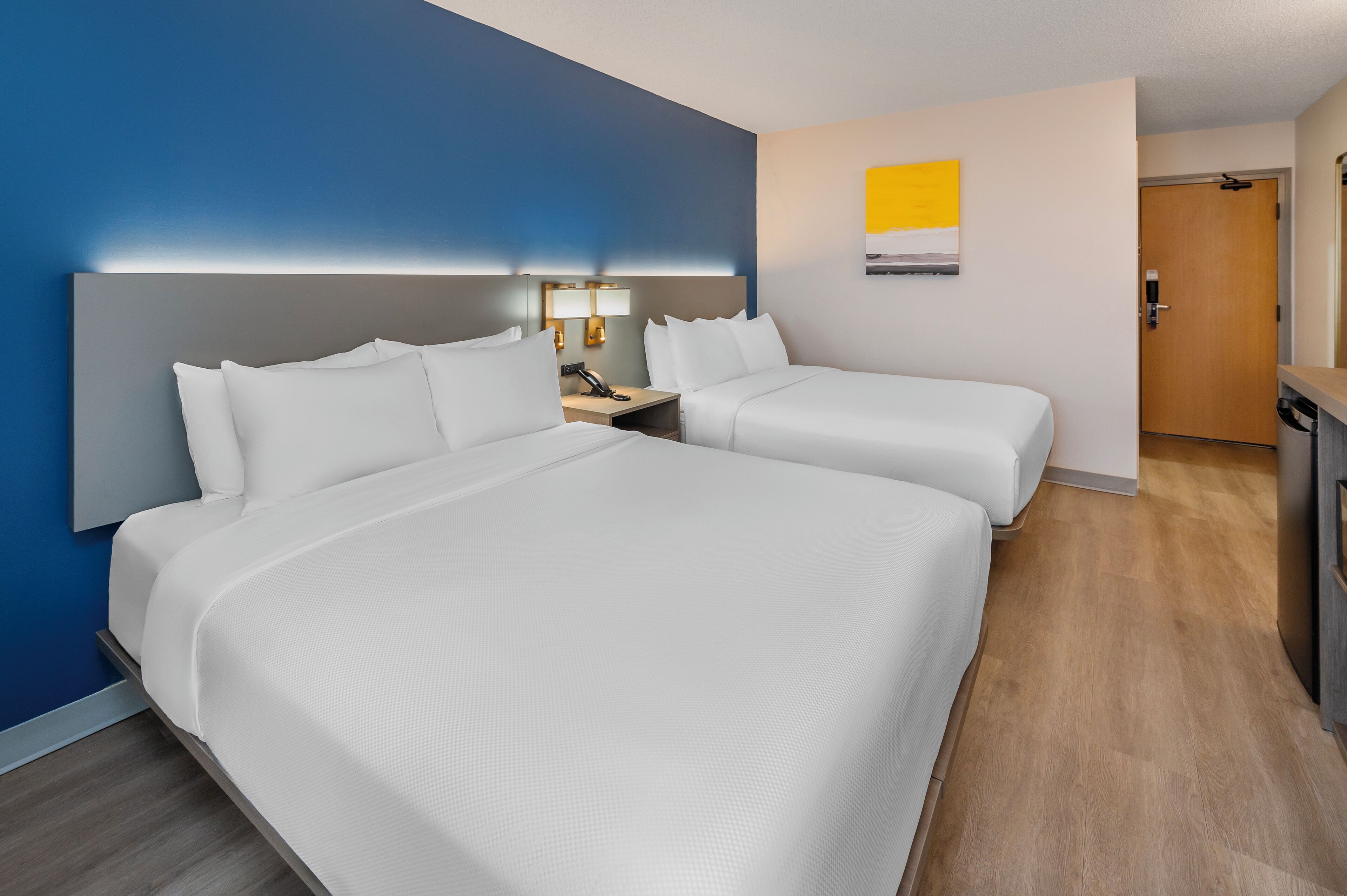 Een hotelkamer met twee bedden, een nachtkastje met een lamp en een deur naar de badkamer.
