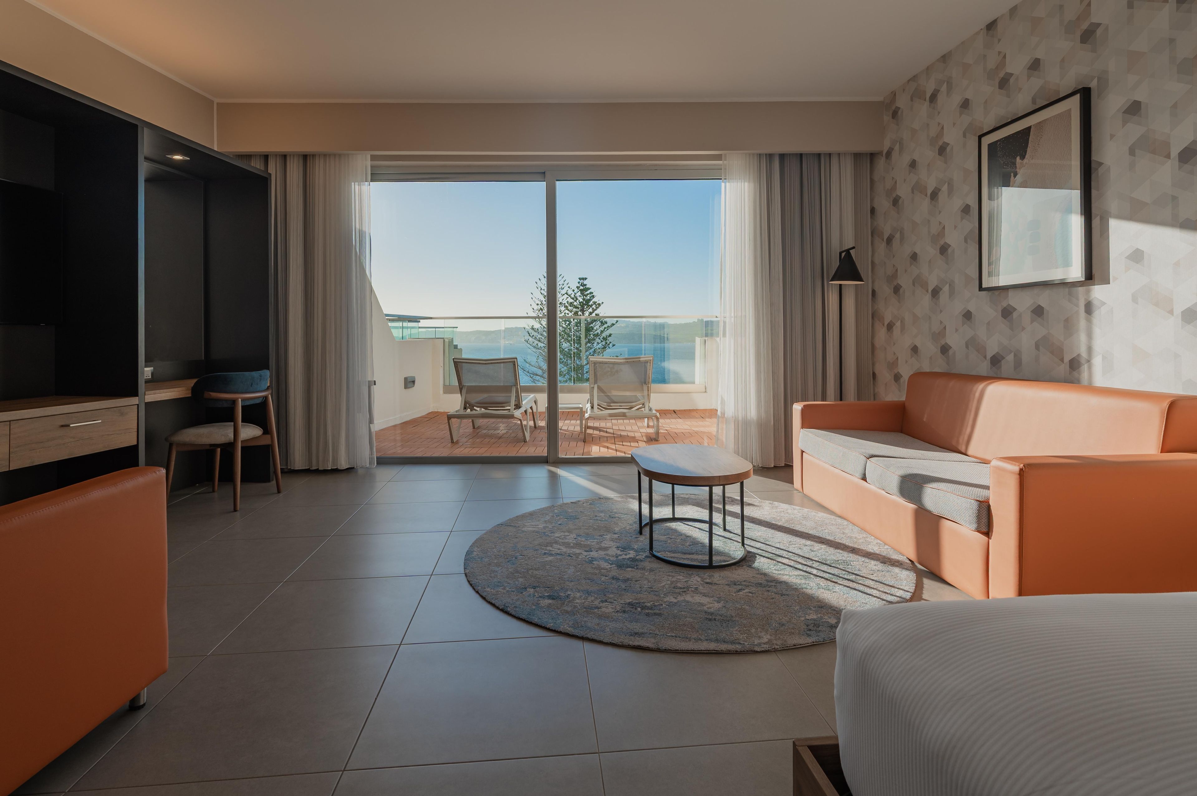 Una moderna camera d'hotel con balcone, un divano, un tavolino e una televisione.