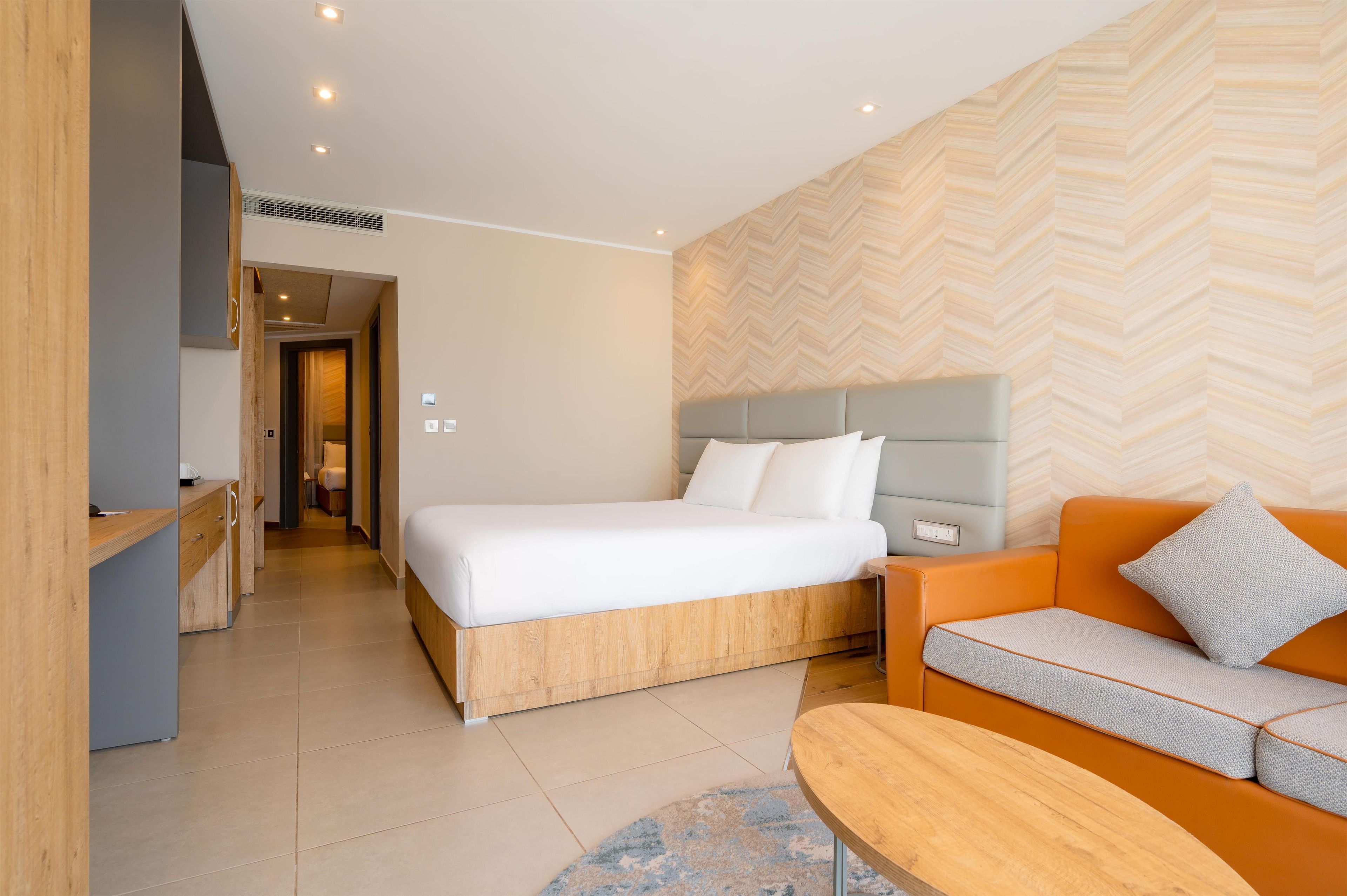 Habitación de hotel moderna con una cama grande, un sofá, una mesita de madera y una pared con estampado de espiga.