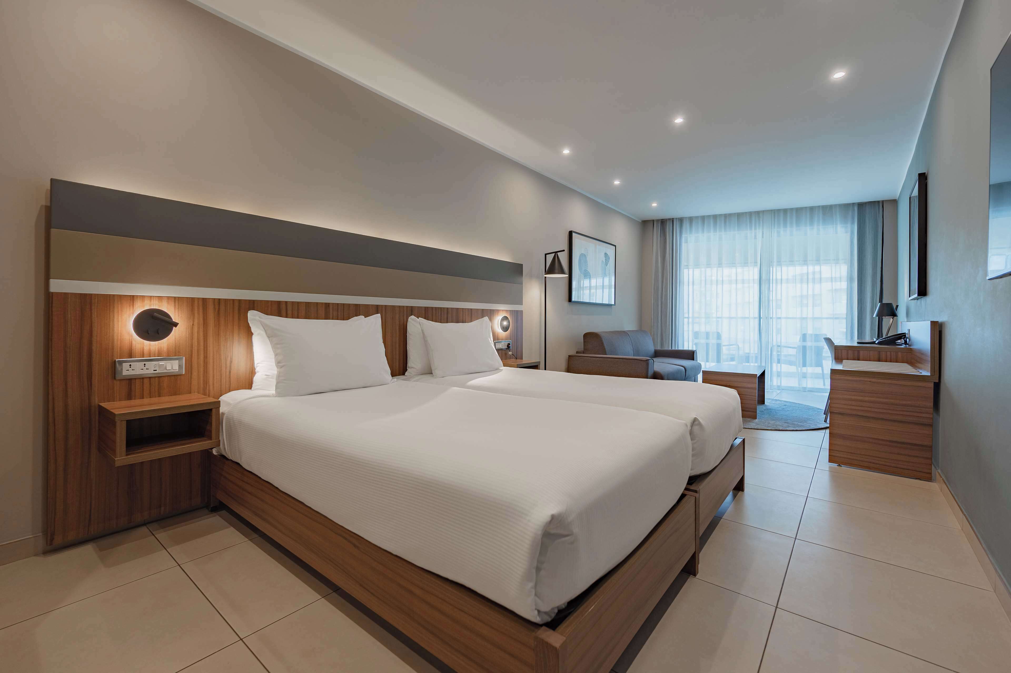 A modern hotel room with a large bed, bedside tables, a desk, and a chair.