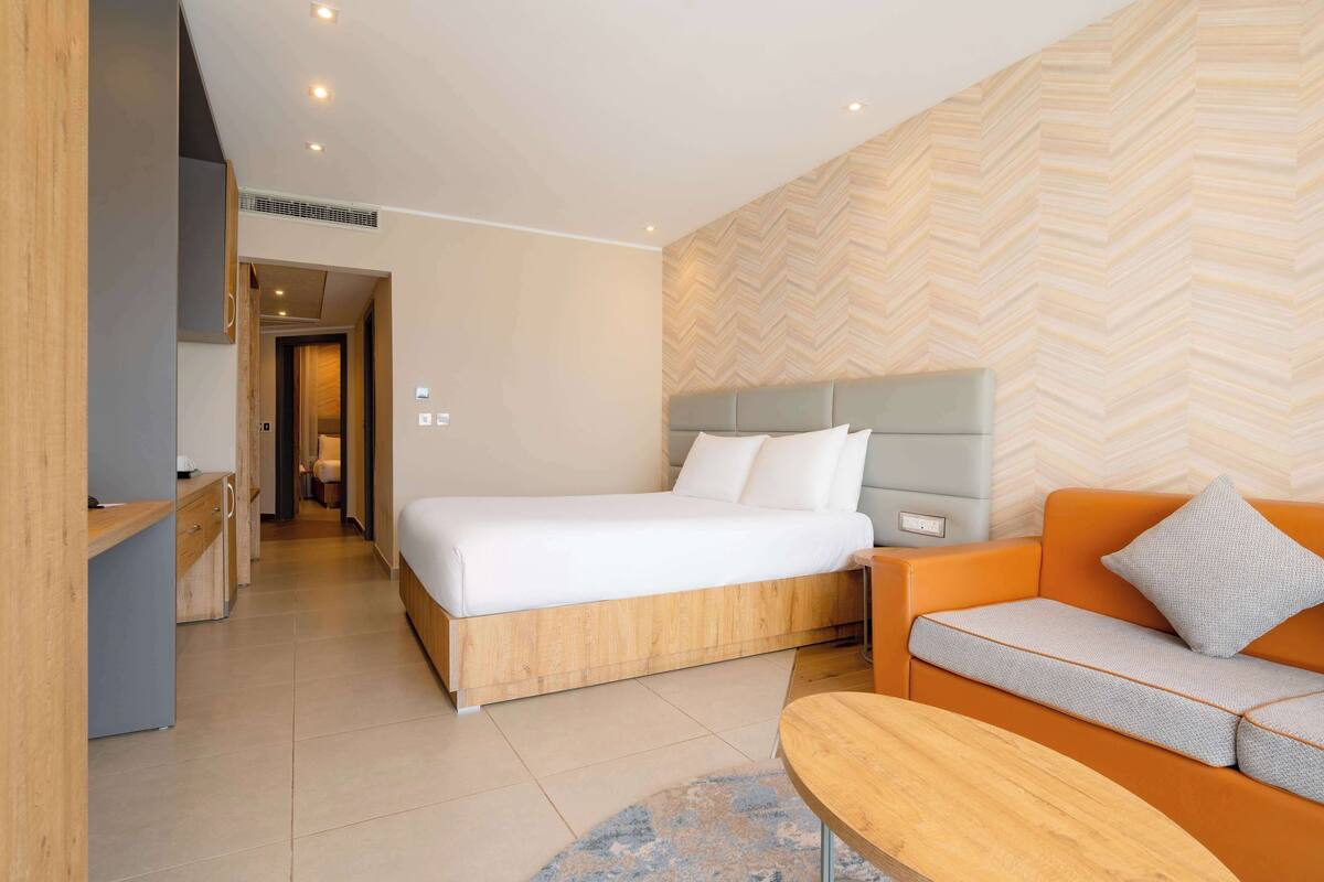 Una habitación de hotel moderna con una cama, un sofá, un escritorio y una pared con estampado de espiga.