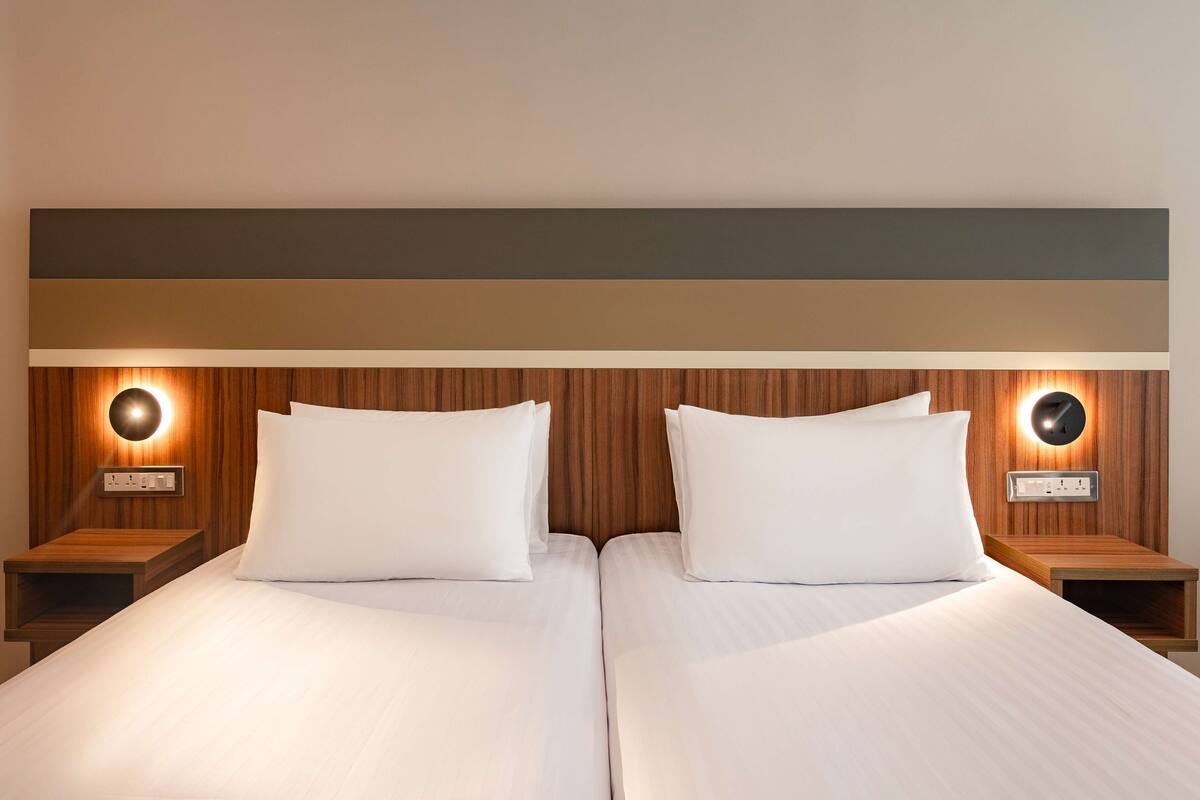 Una cama doble con ropa de cama blanca, dos mesitas de noche con lámparas integradas y un cabecero de madera.