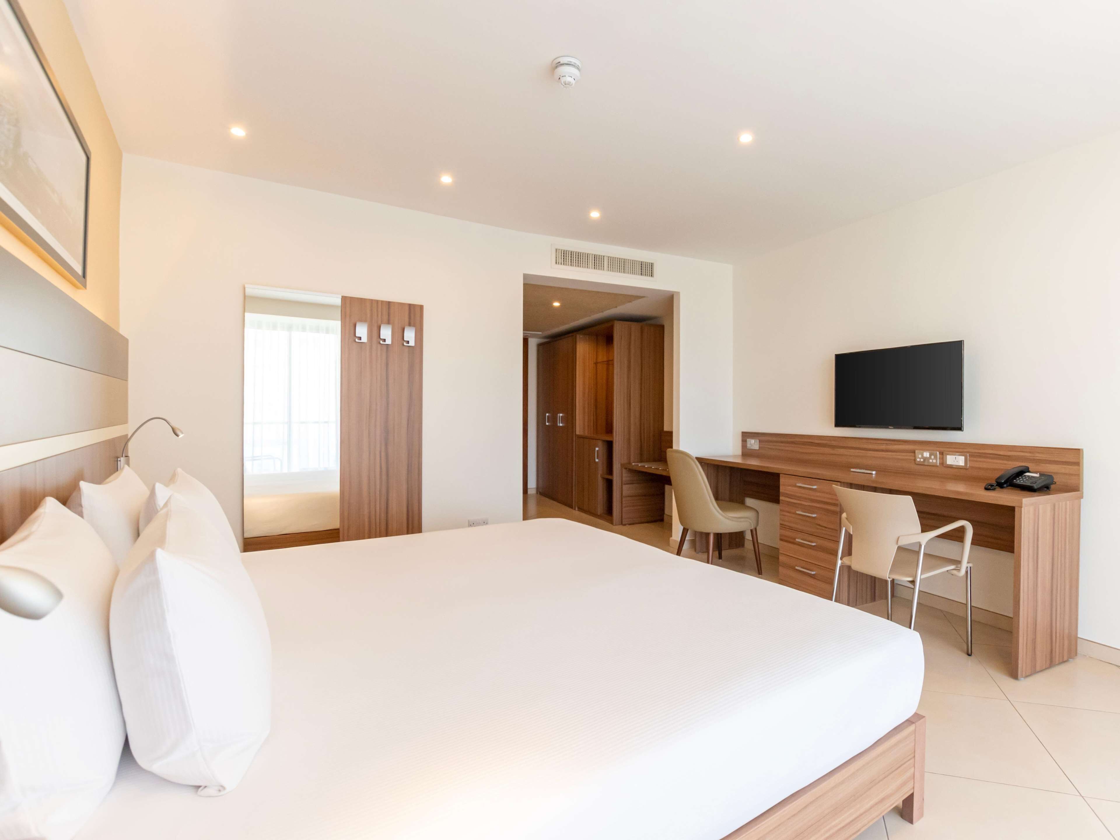 Een hotelkamer met een groot bed, een bureau met stoel, een televisie en een kledingkast.