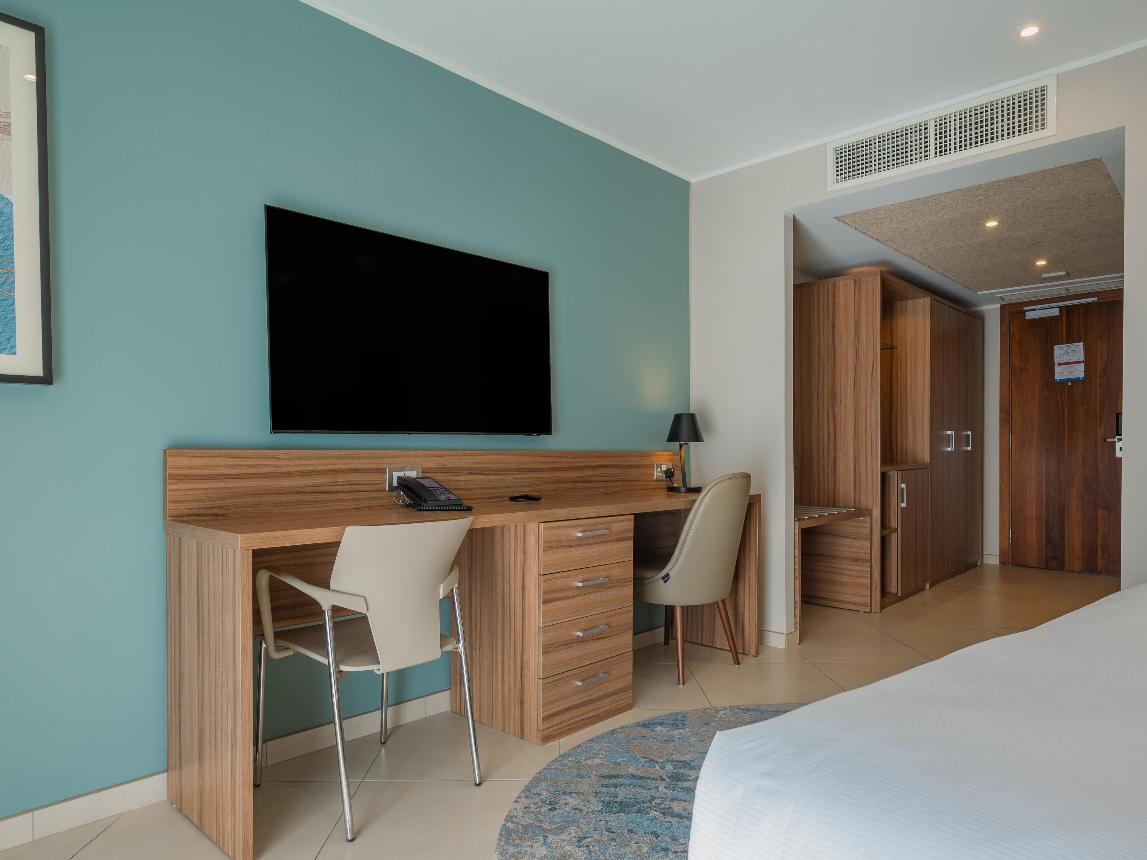 A hotel room with a bed, a desk with a chair, a television, a wardrobe, and a bathroom.